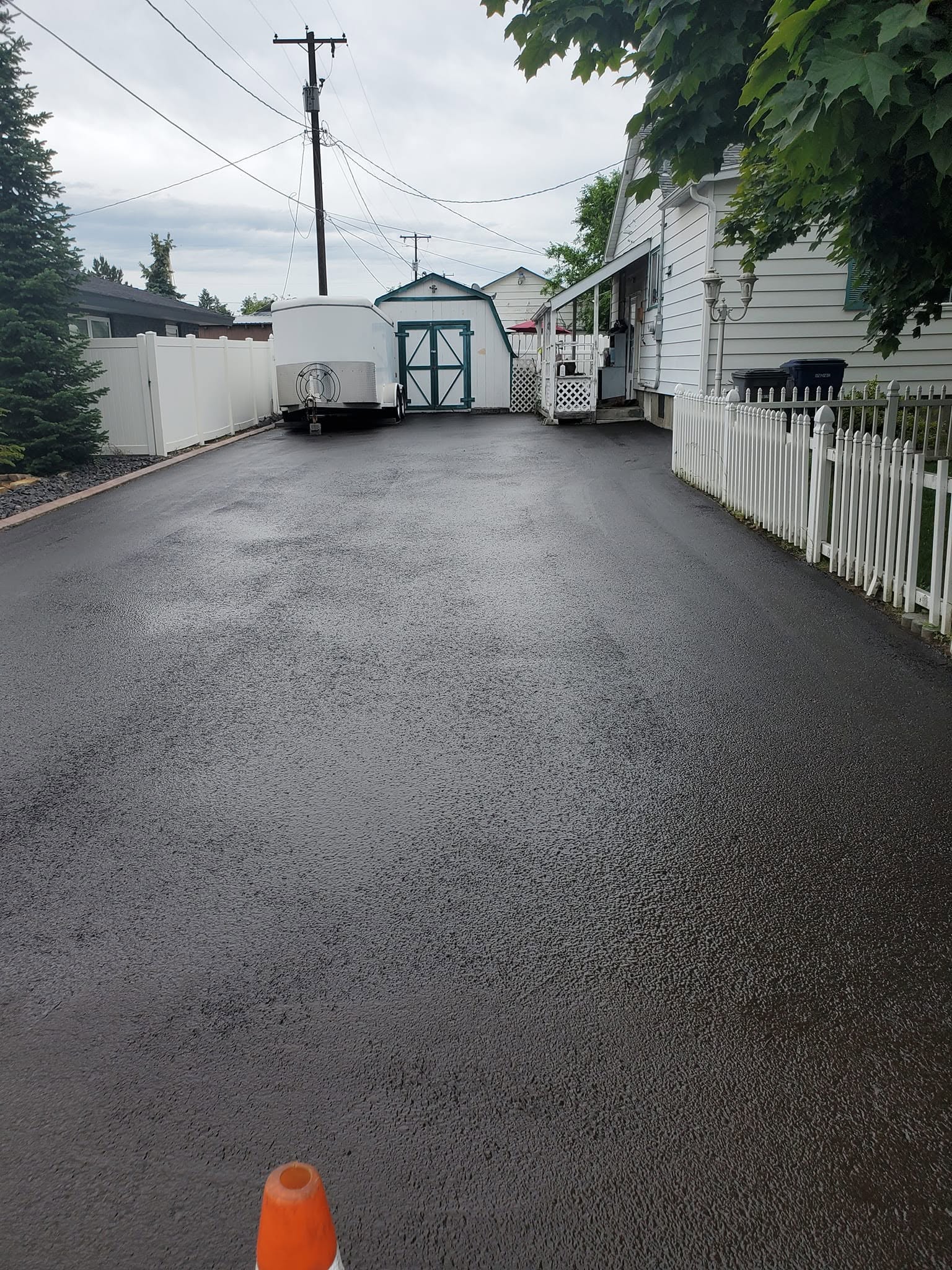 Sealed residential driveway beside a white fence and home.