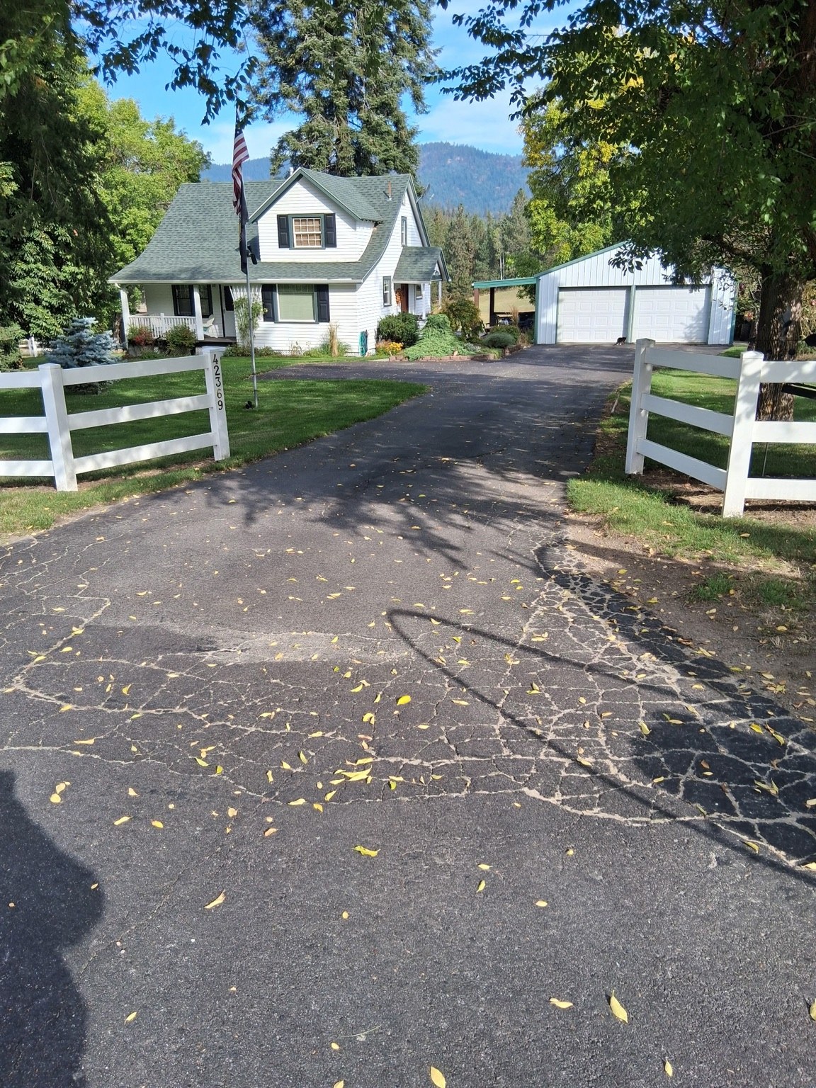 Residential driveway leading to a home and garage, bordered by white fencing.